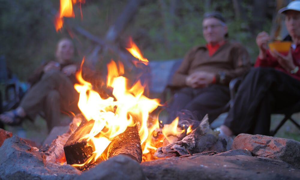 people stare into a small fire while sitting in camp chairs