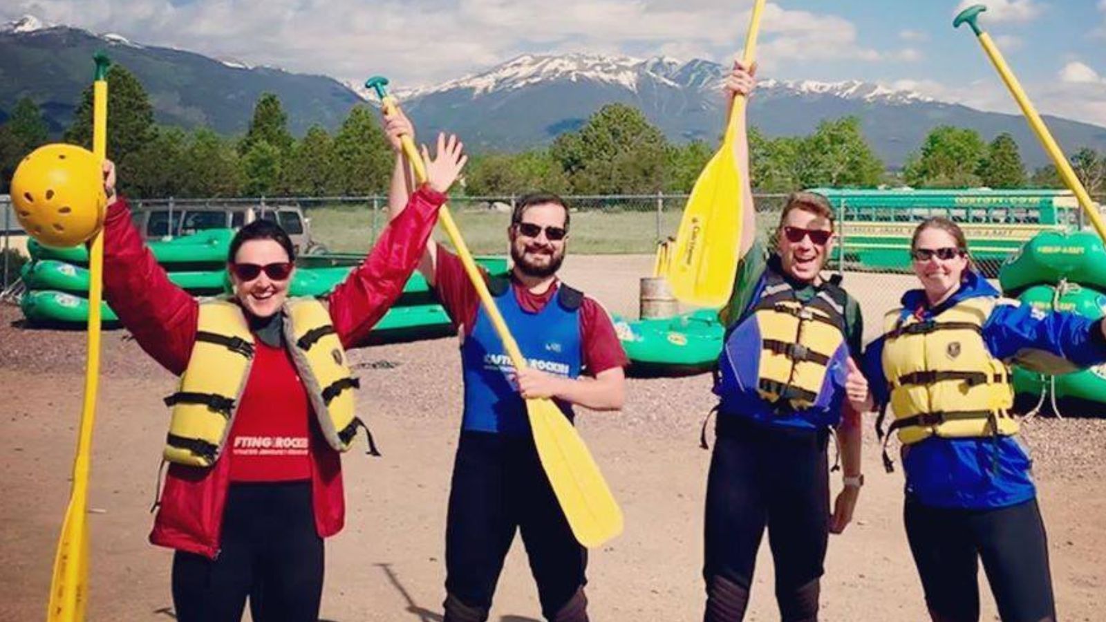 Four people in white water rafting gear raise their hands in the air