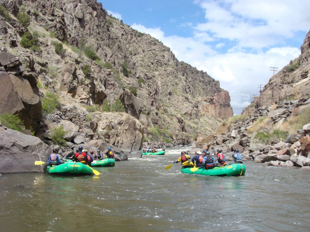 four rafts with people take turns will navigating a narrow river section