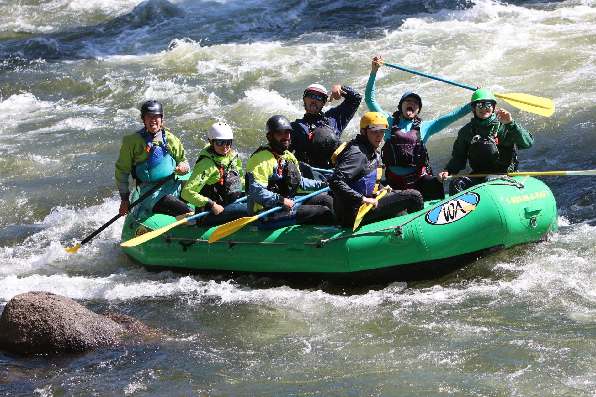 people on a green raft smile and make faces while on a river