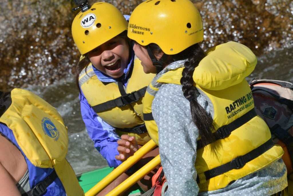 two girls on a raft wearing yellow helmets and yellow life vests