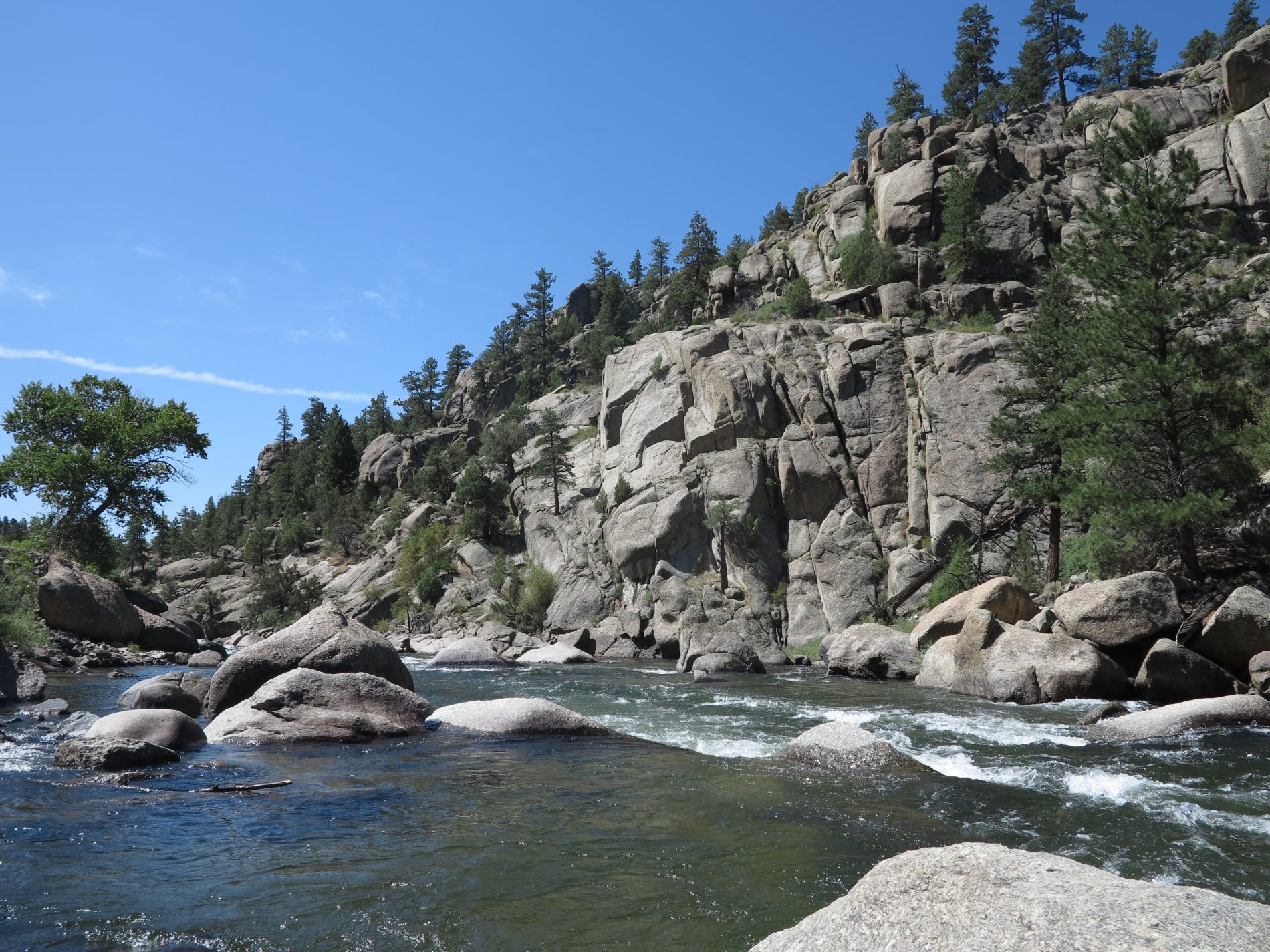 a river flows through a rocky canyon on a blue sky day