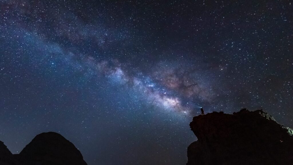 A person in a headlamp looks at the milk-way at night