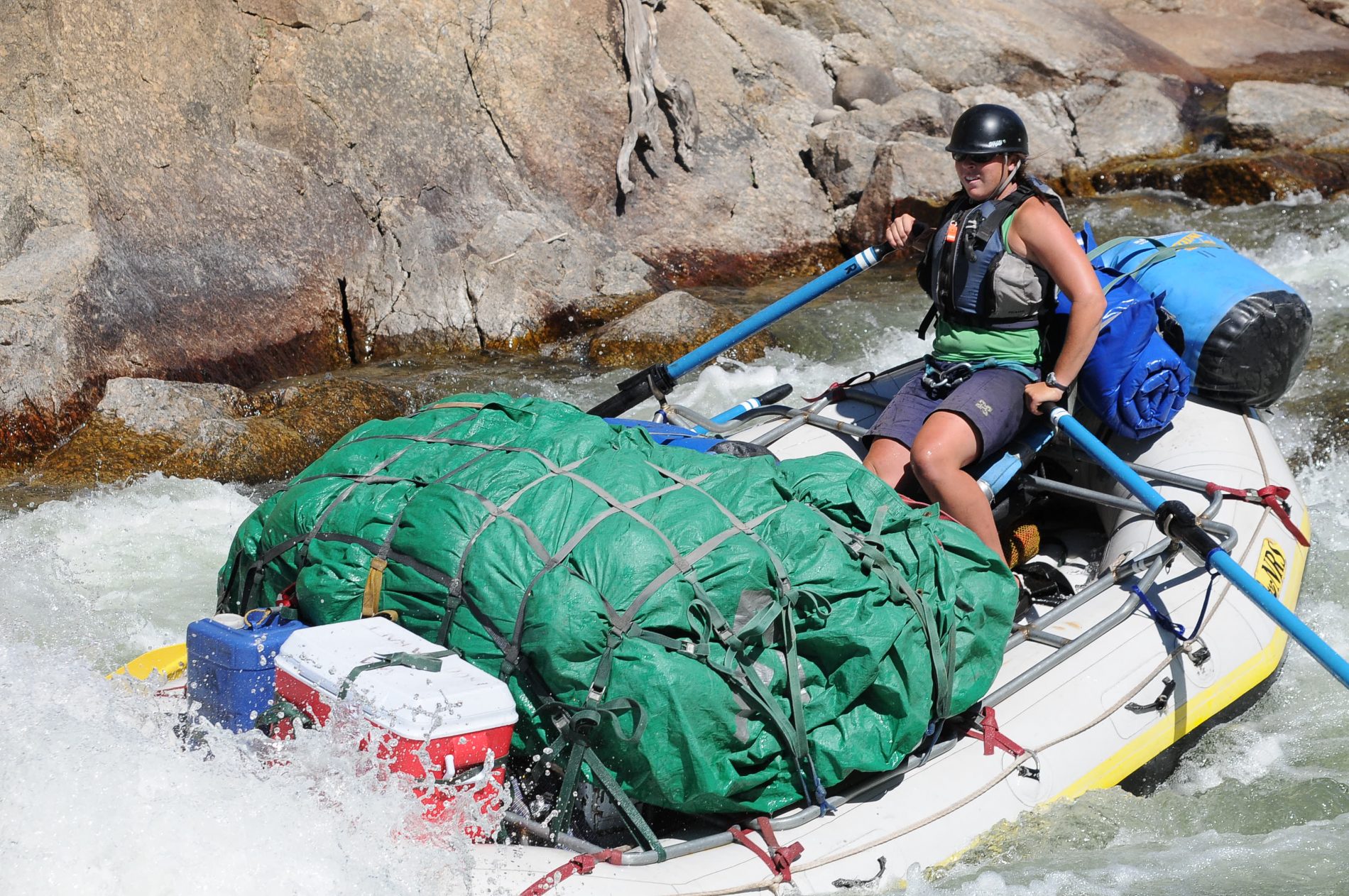 A river rafting guide on a pack raft paddling through rapids.