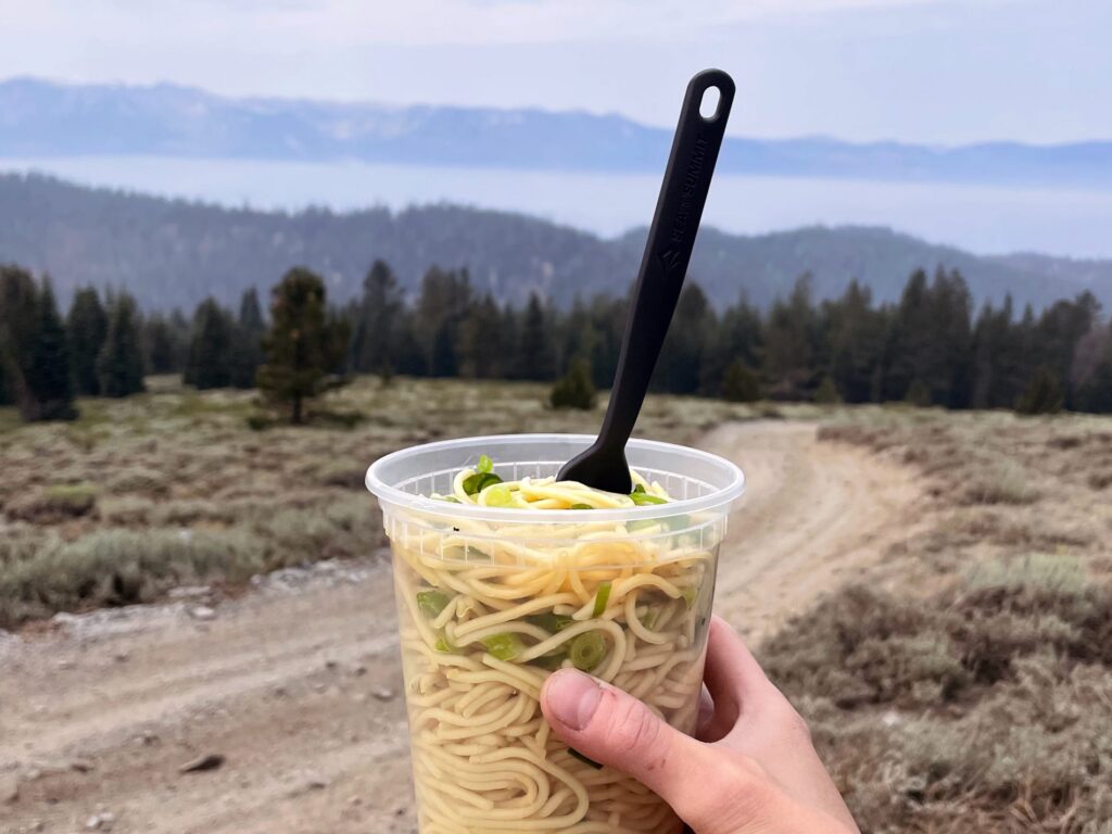 a person holds up a homemade pasta salad in a plastic container