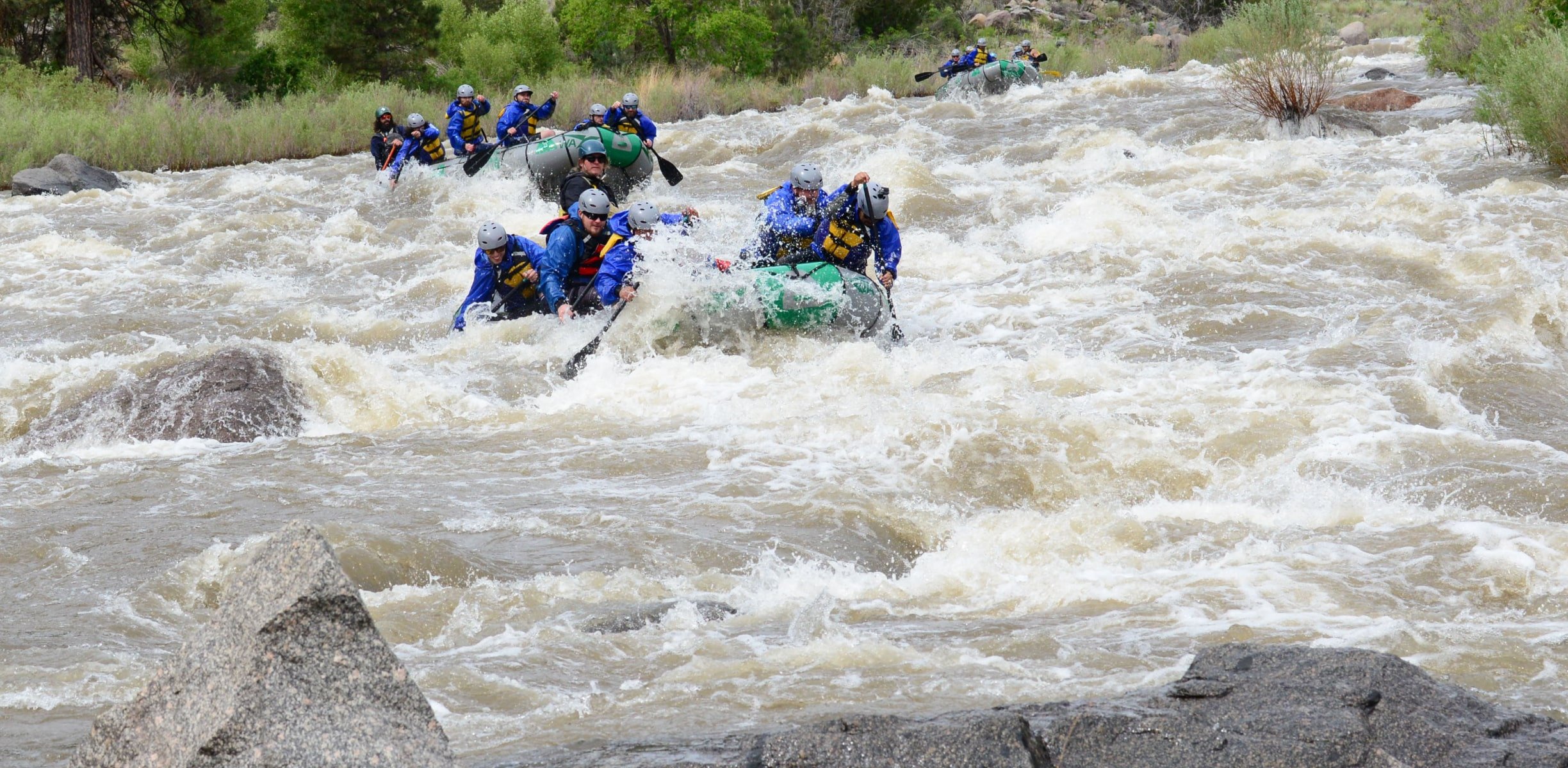 Several rafts full of people navigating a river with rapids