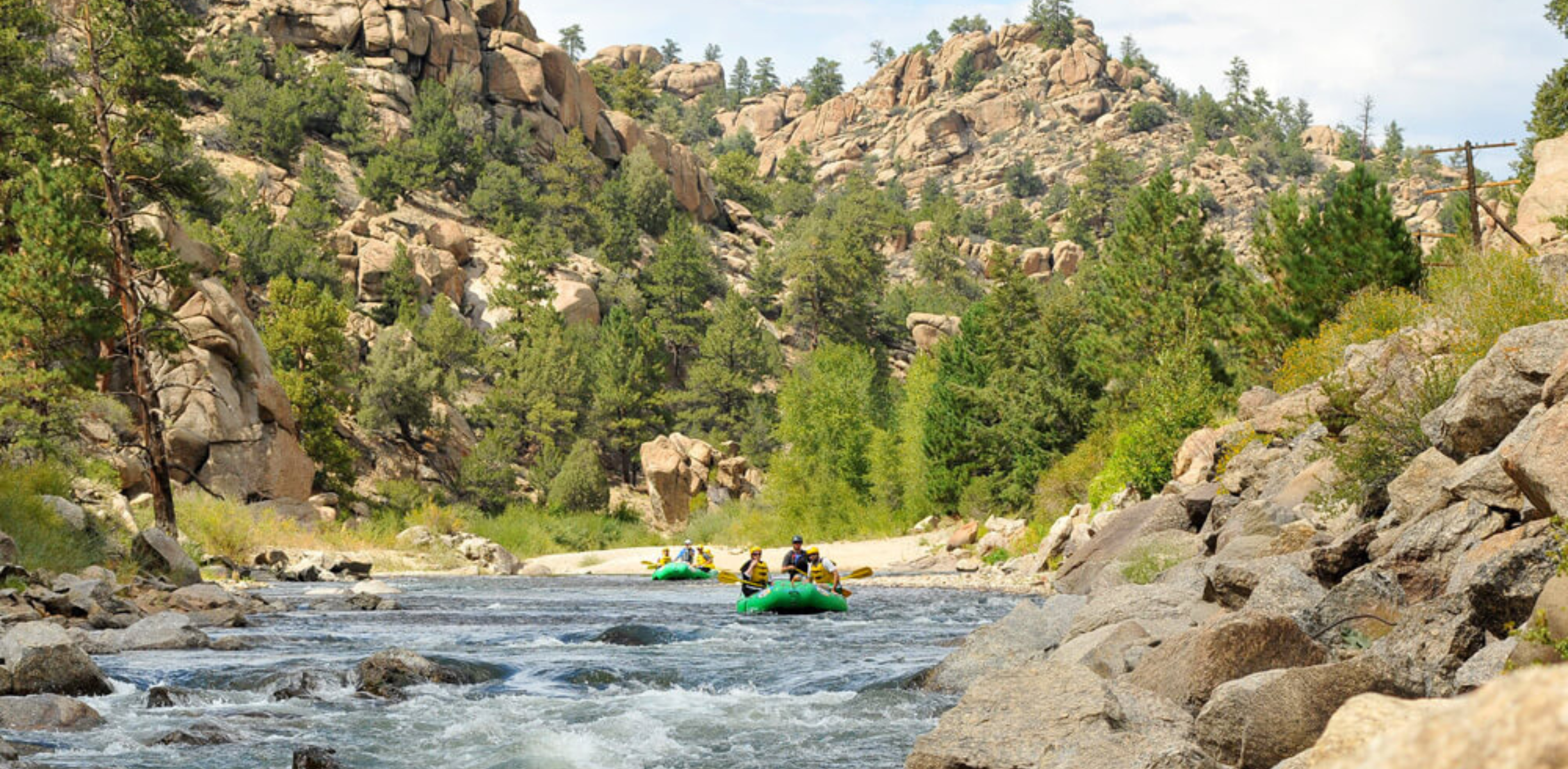 A green raft rows through rapids on a river