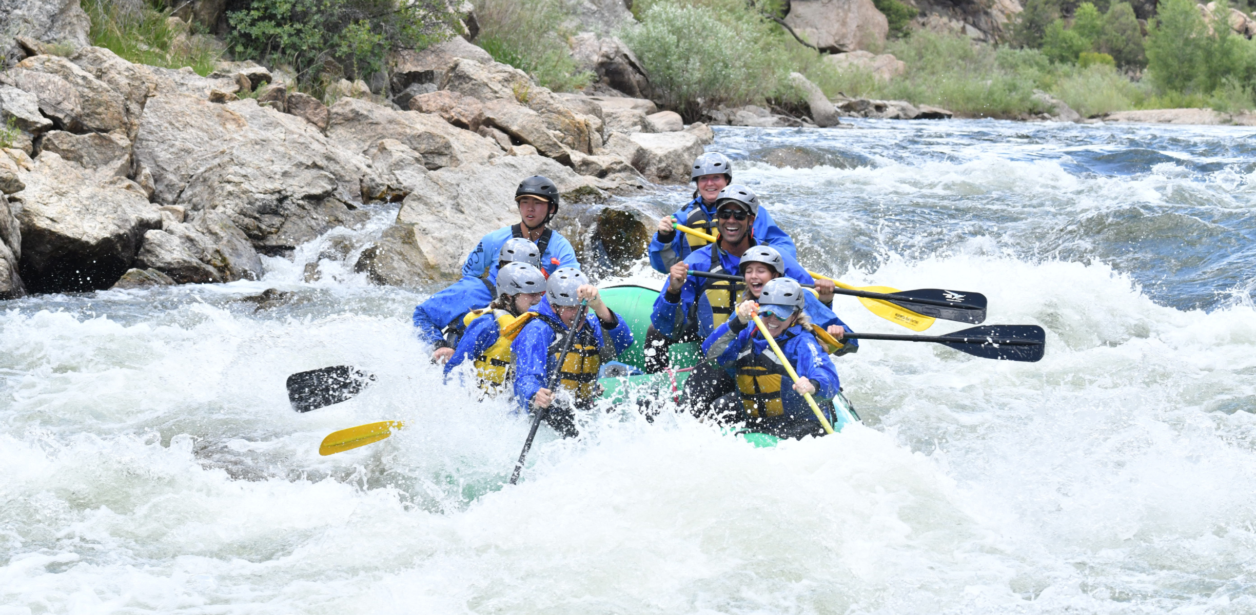 A group of people on a raft paddle through thrilling white water