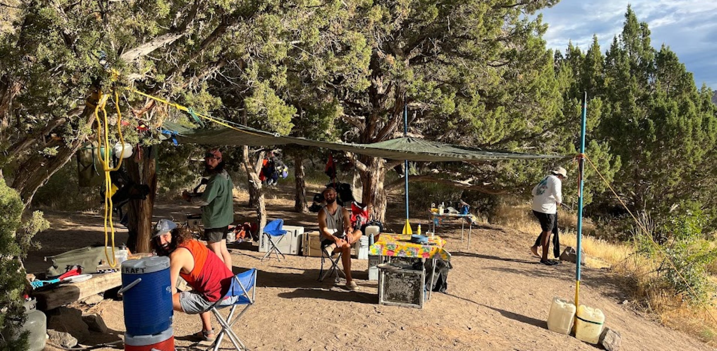 A group of campers smiling under a canopy at river camp, enjoying the morning sun during an overnight rafting trip in Colorado.