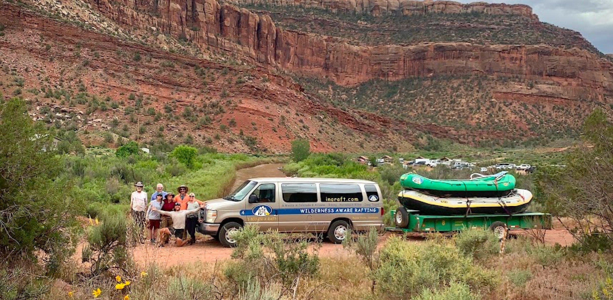 Raft guide smile and pose next to their van with two rafts stacked on the trailer