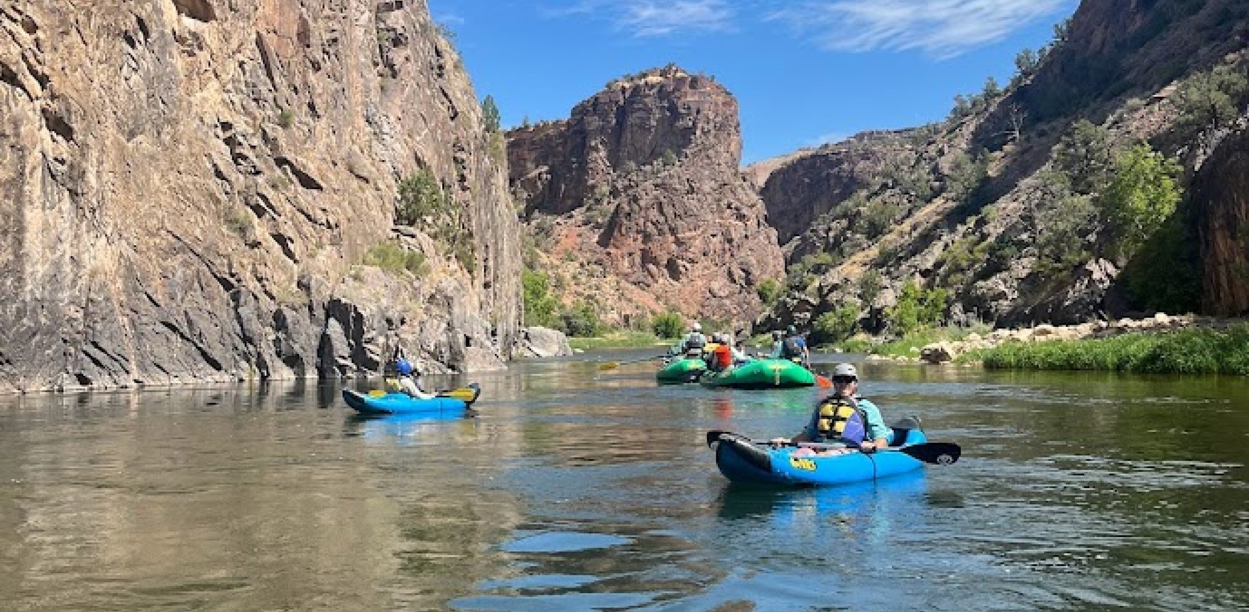 Folks kayaking and rafting in a scenic river canyon