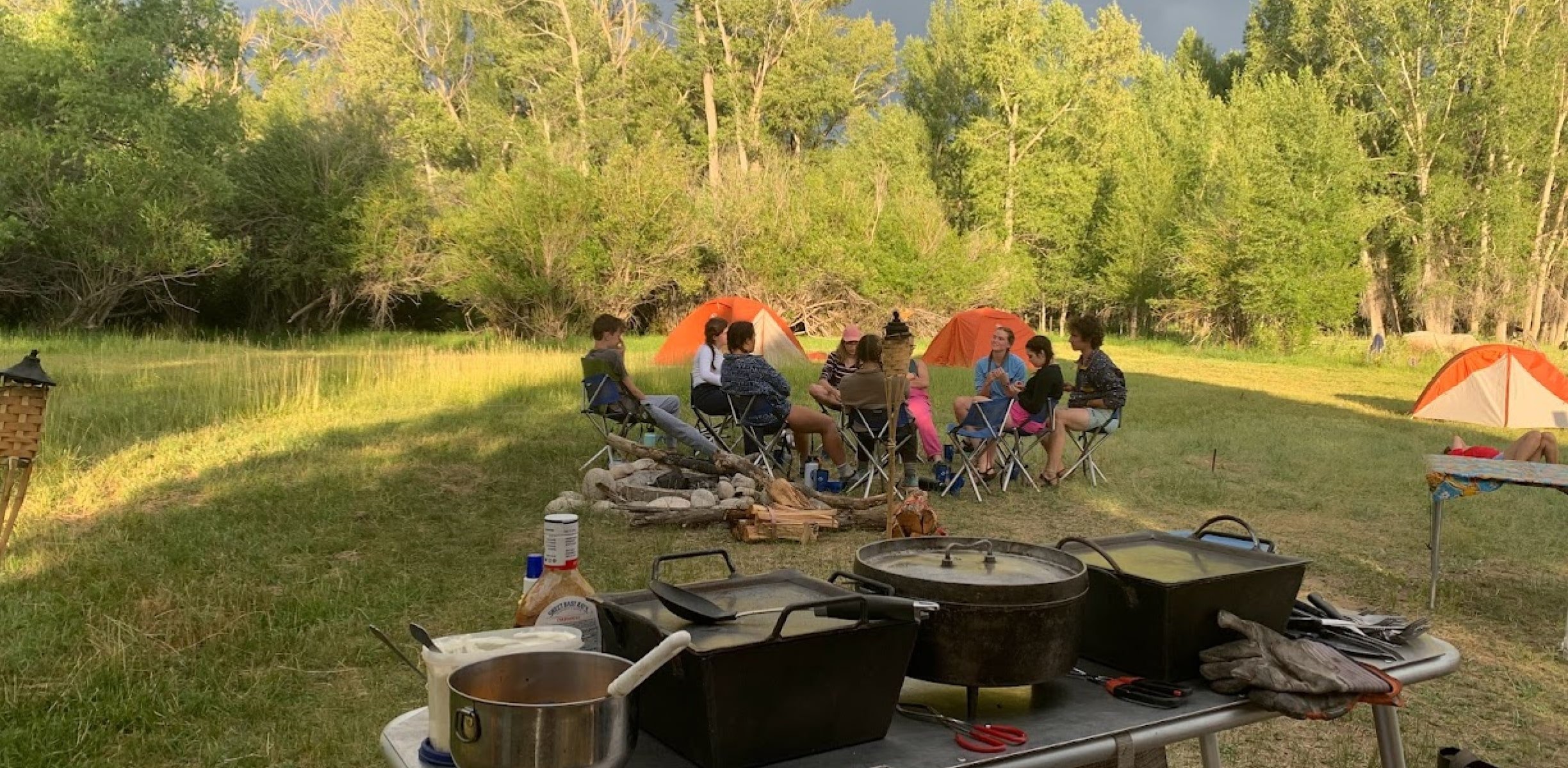 People sitting around a circle in camping chairs with orange tents in the background