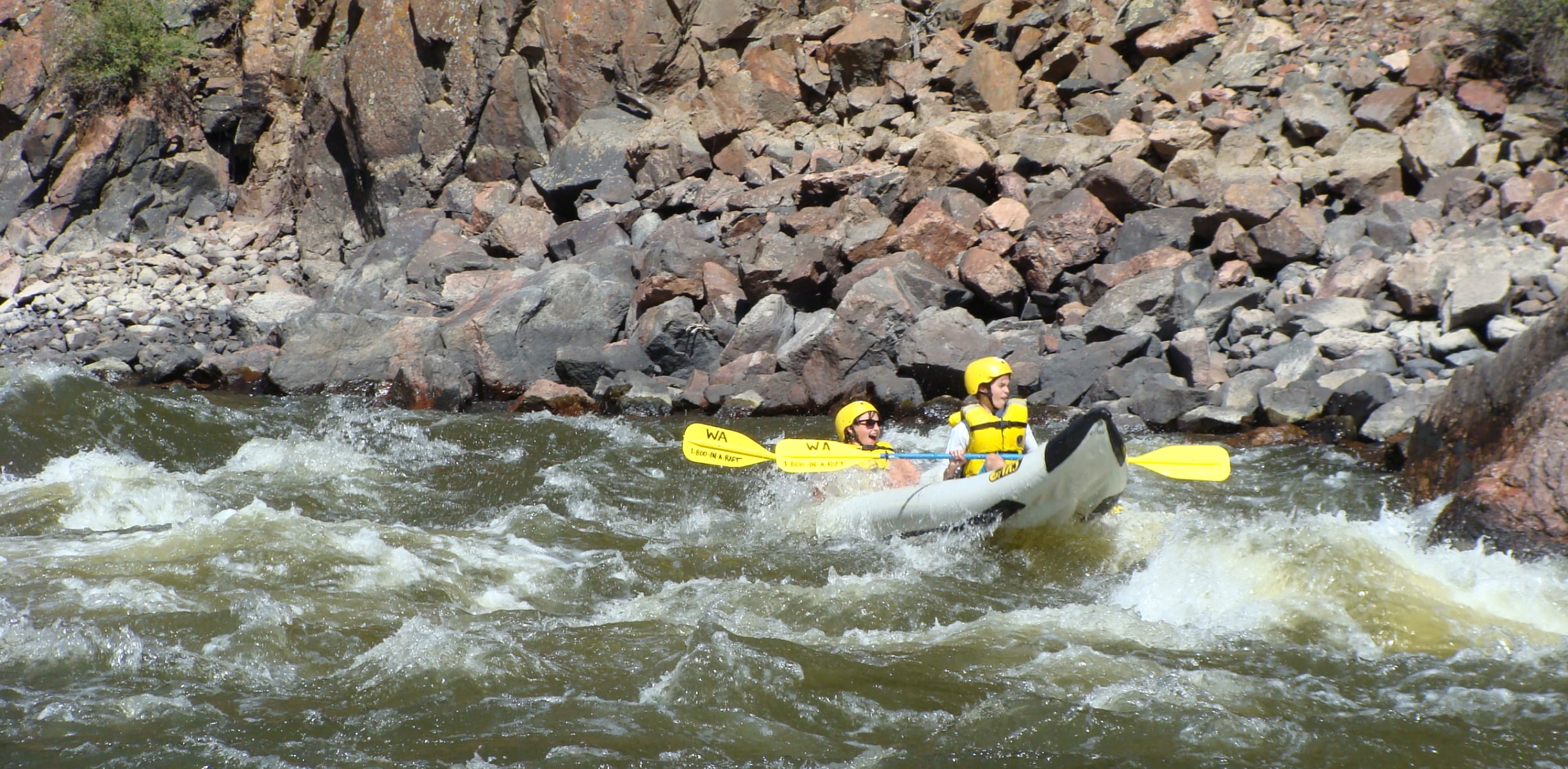 Two kids paddling an inflatable kayak through white water rapids