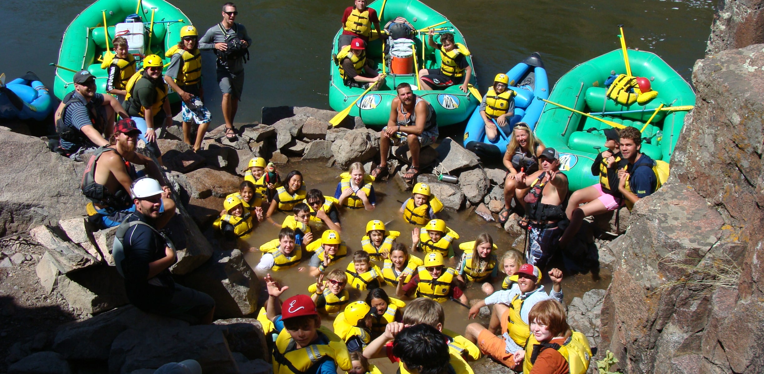 A group of kids in life jackets in natural pool on the side of the river