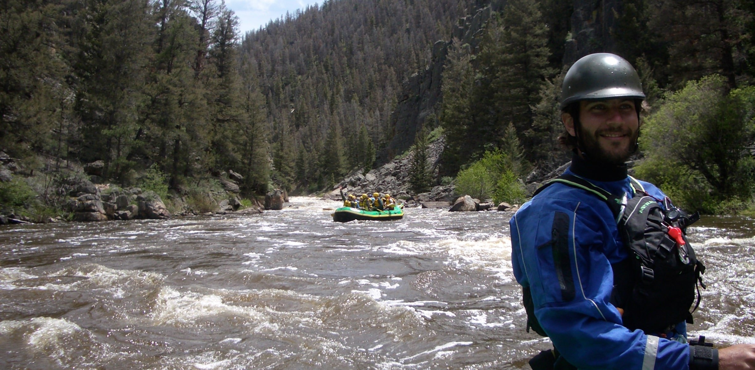 A man posing in the back of a raft, while another raft comes down the river.