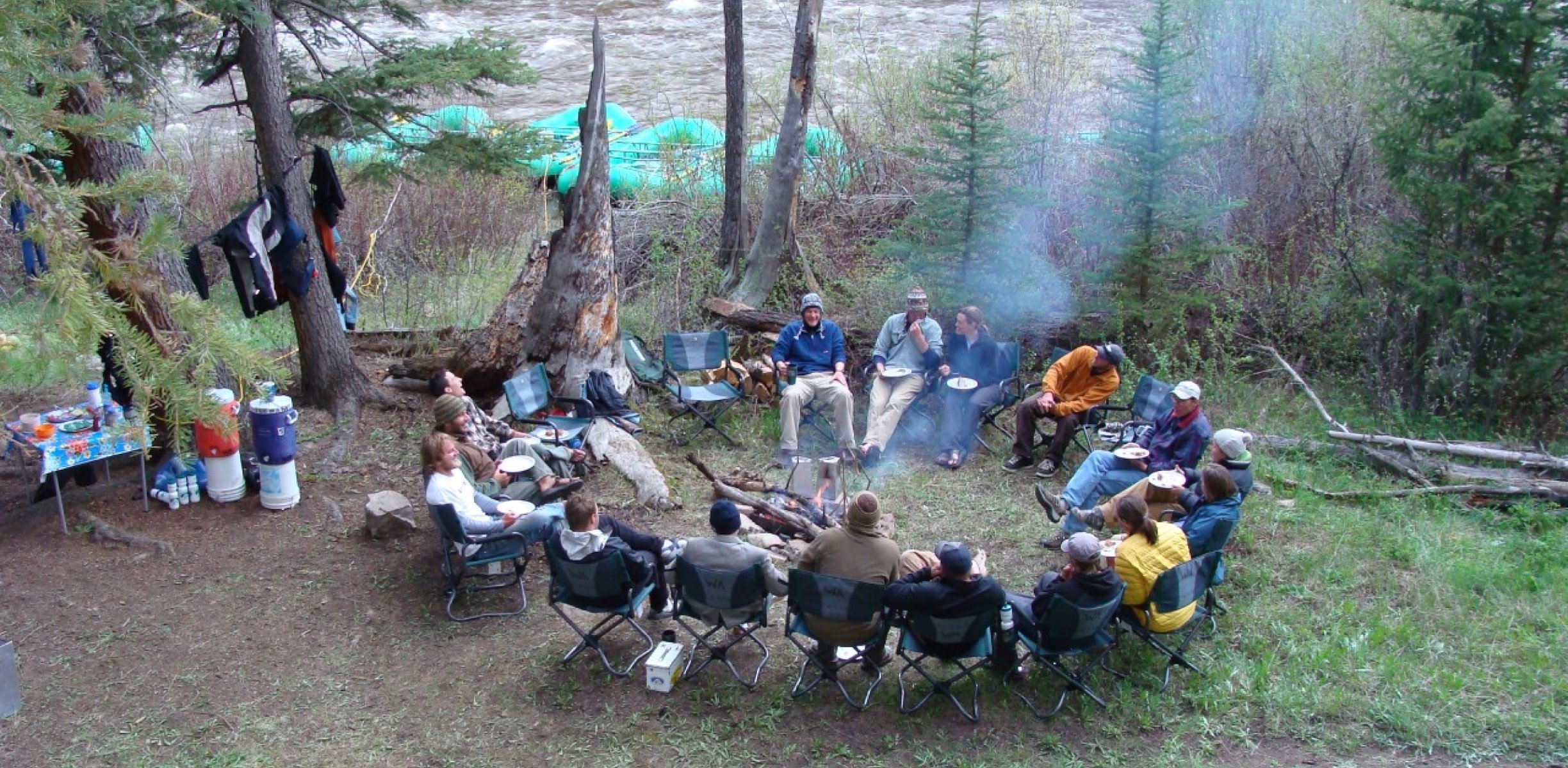 Group of campers sitting around a campfire enjoying a meal on the riverbanks during an Arkansas River multi-day rafting trip.