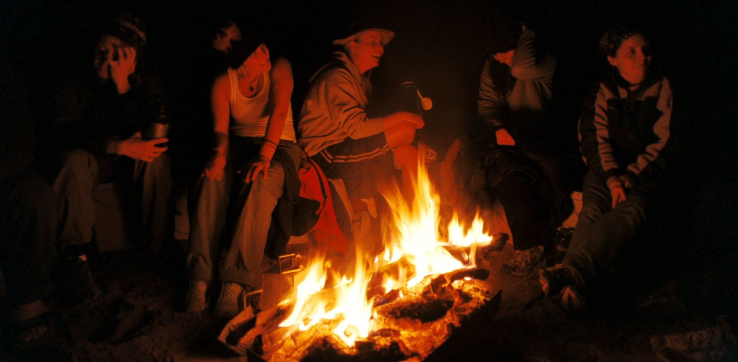 People hanging around a campfire in the dark.