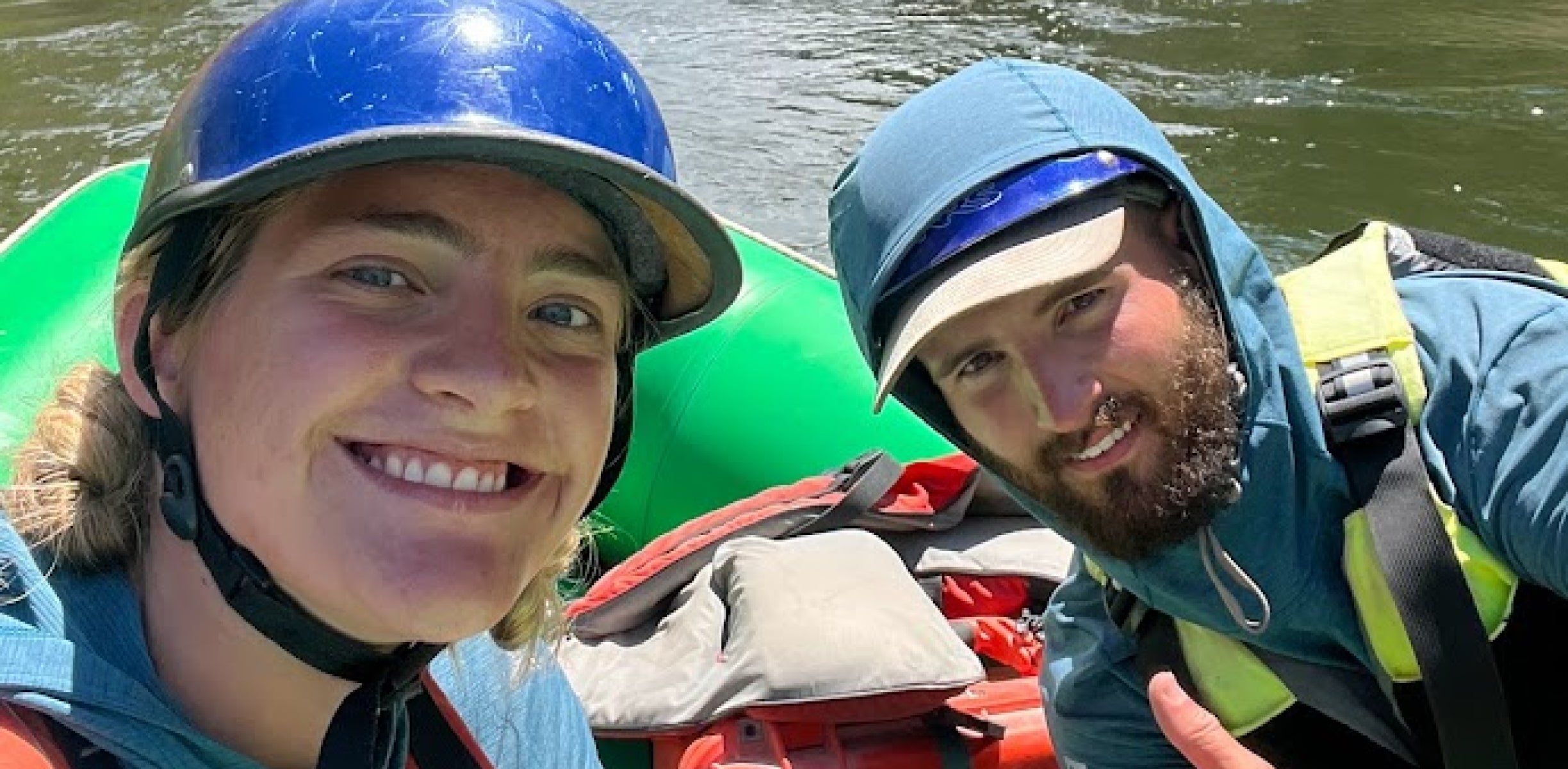 Two people taking a selfie while rafting on a green boat on the river