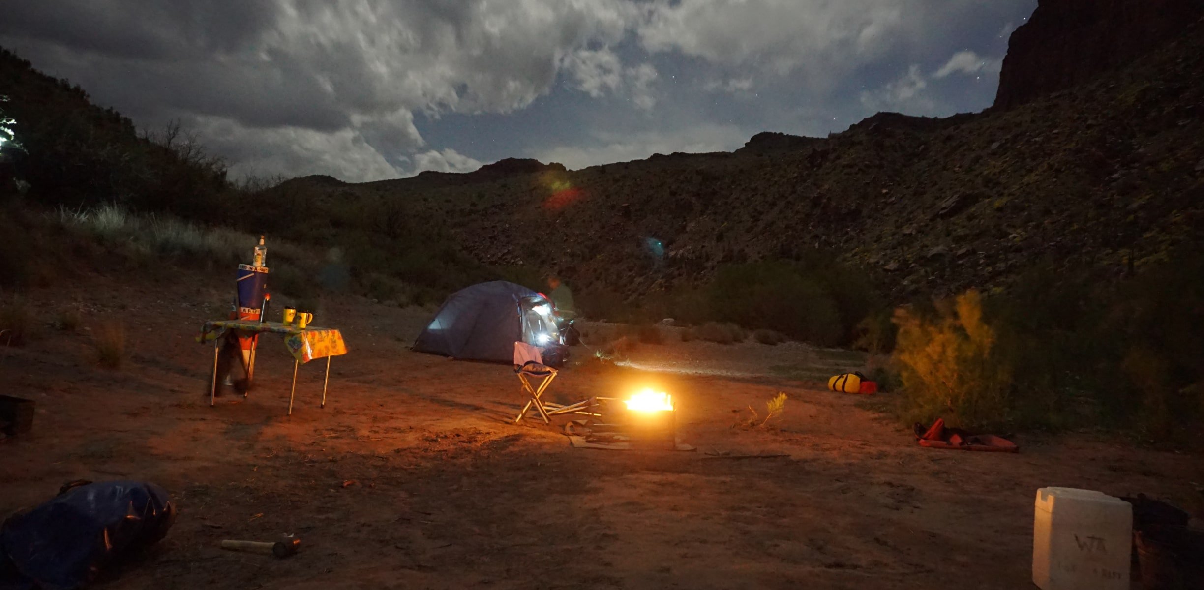 A photo taken at night of a camp next to the river and light from a fire