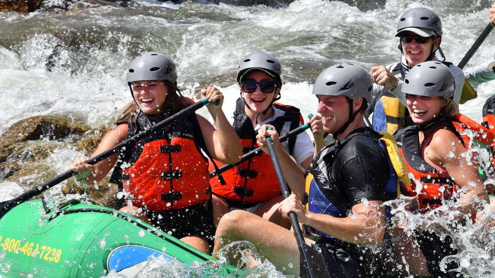 A green boat filled with people laughing while white water rafting