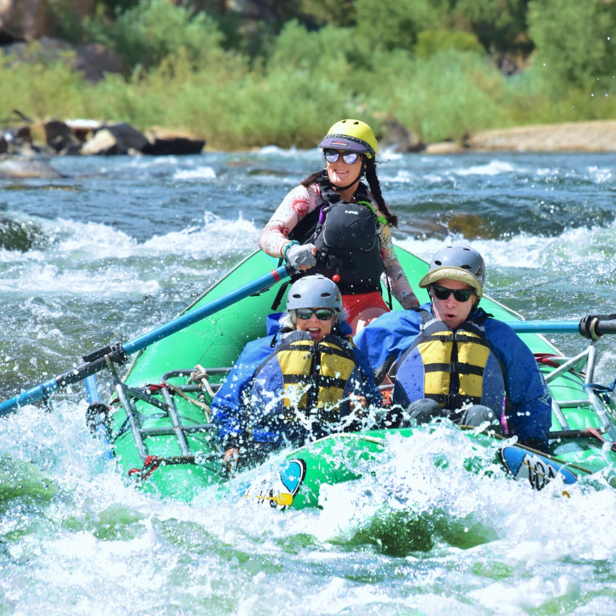 Three people hitting a wave in a raft