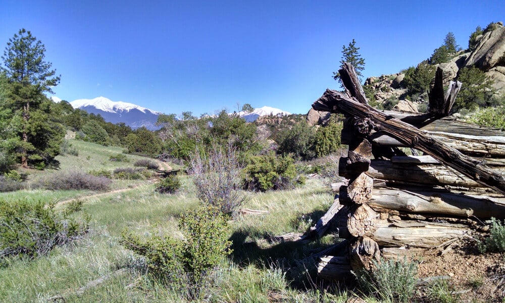 Historic structure from the 1800s framed by the Browns Canyon monument and snowcapped mountains in the background, showcasing the rich history and stunning scenery experienced on rafting trips in Colorado.