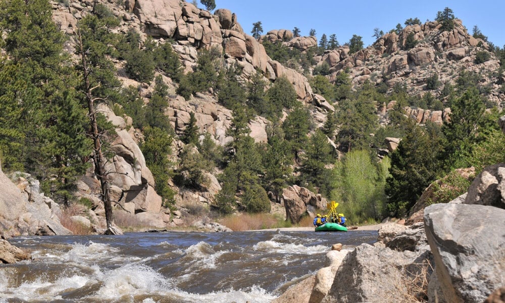 A group of people rafting in Browns Canyon and celebrating with their paddles raised in the air