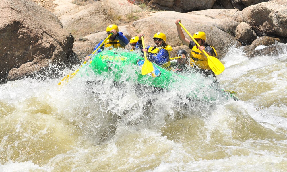 A raft full of people hitting a massive wave in the middle of a river