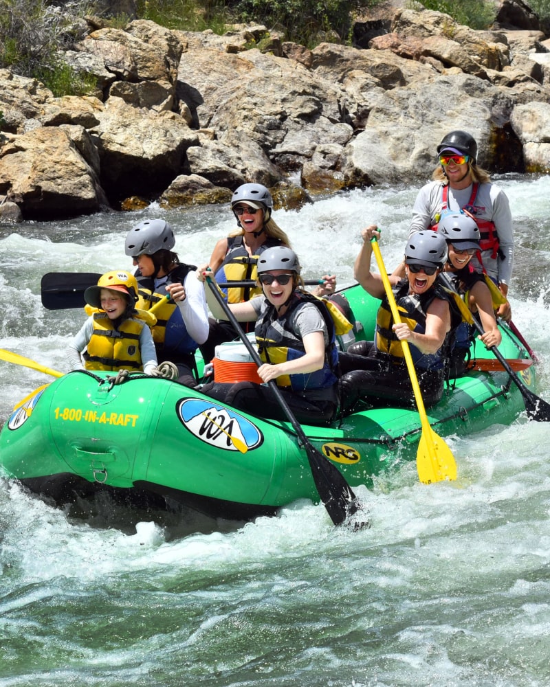 a green boat with 7 laughing and happy people holding oars