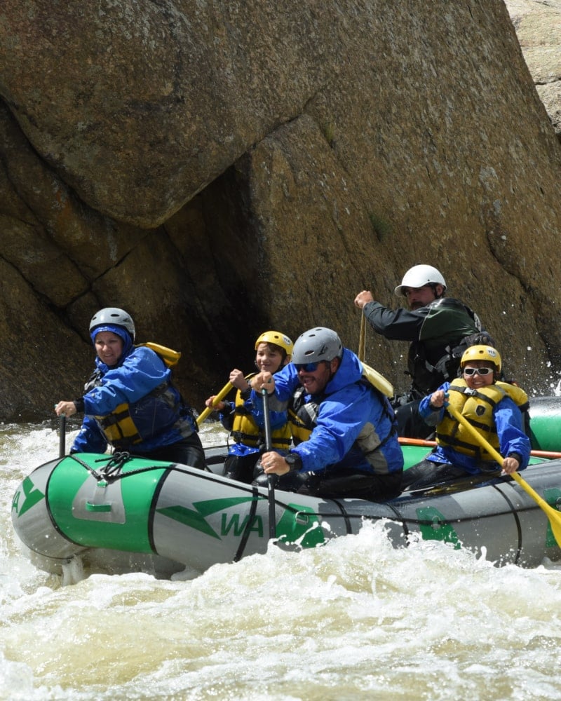 A family rafting passes boulders while going through rapids on the Arkansas River in Colorado.