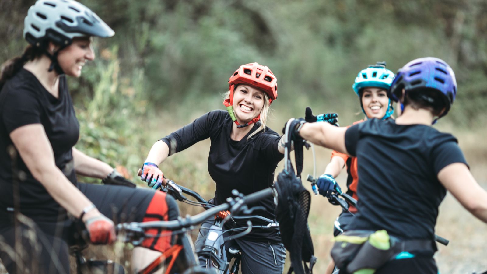 Four women in mountain biking gear stand near their bikes and laugh