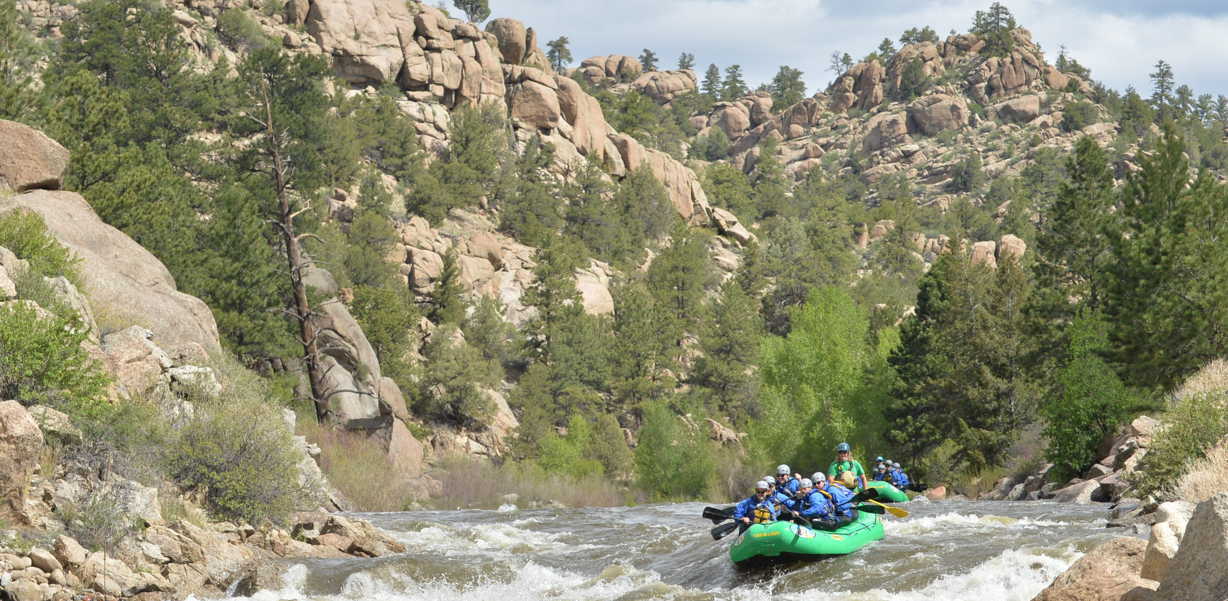 People in a green raft navigate a scenic and rocky stretch of river