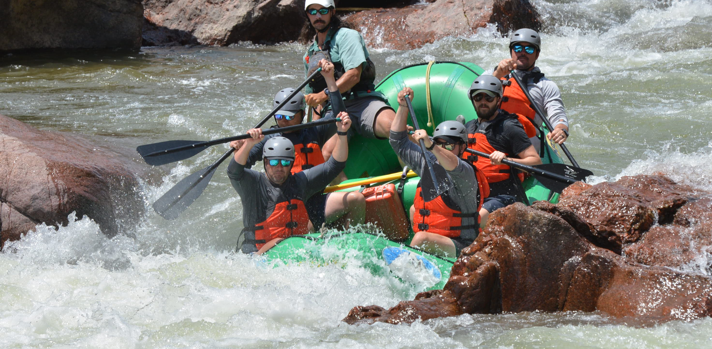 People in a green raft navigate a rocky section of white water rafting