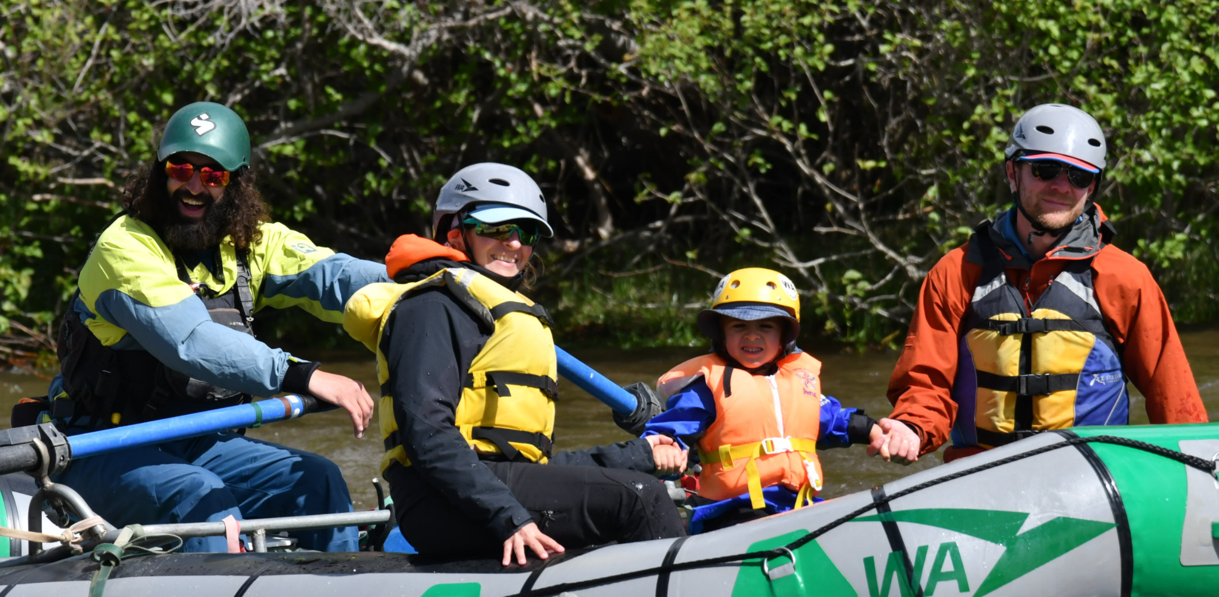 A family of three smile on a raft during a mellow stretch of the river