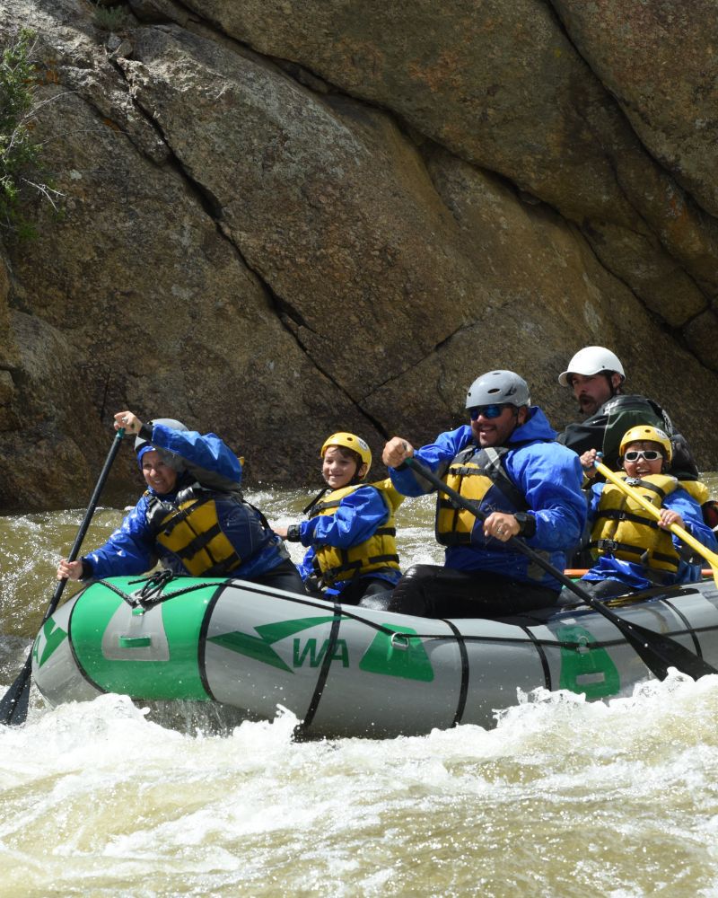 A family in a green and grey raft with a river guide